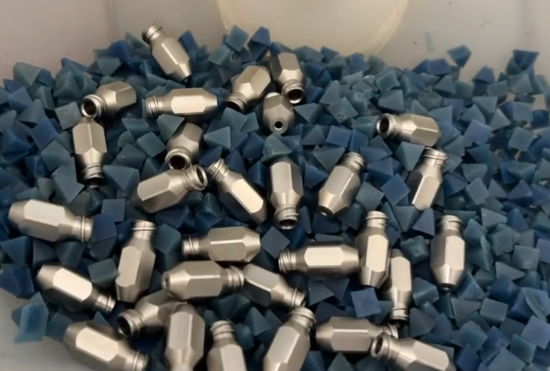 Tumbling and Deburring of Metal Components Batch of small machined metal parts being polished inside a tumbling container with abrasive media